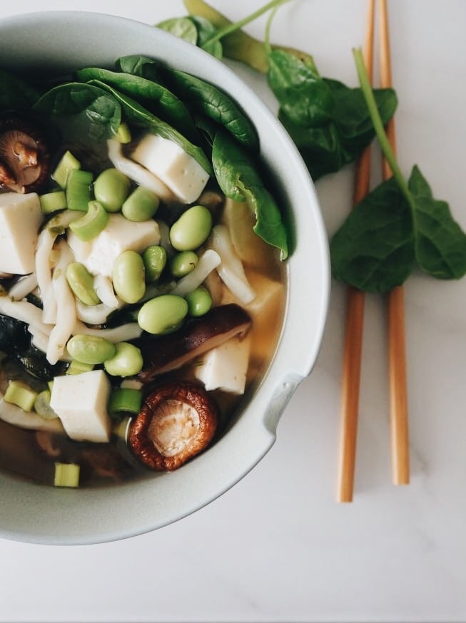 Vegane Miso-Suppe mit Udon-Nudeln, Gemüse & Shiitakepilzen. Dekoriert mit Frühlingszwiebeln, Edamame, Babyspinat und Essstäbchen.